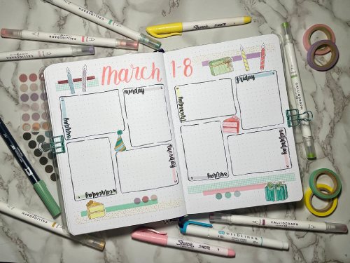 Open weekly bullet journal spread with stationery supplies around. Birthday theme with pastel colors and stickers.