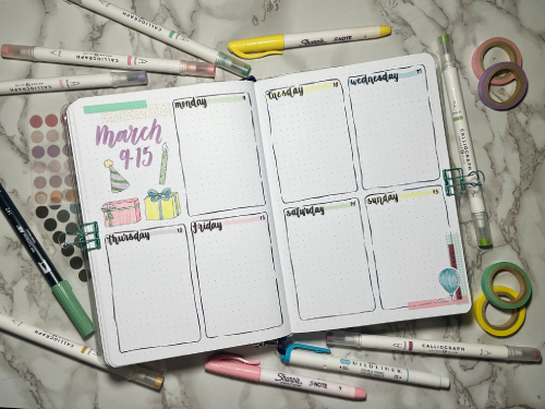 Open weekly bullet journal spread with stationery supplies around. Birthday theme with pastel colors and stickers.