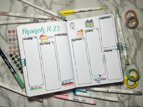 Open weekly bullet journal spread with stationery supplies around. Birthday theme with pastel colors and stickers.