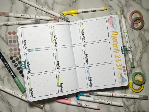 Open weekly bullet journal spread with stationery supplies around. Birthday theme with pastel colors and stickers.